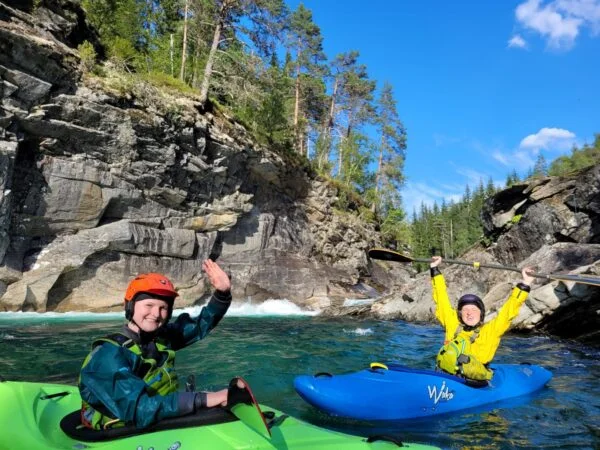 To gruppe deltakere på et grunnkurs i elvepaddling er klare til å sette ut i elven. De har på seg redningsvester og har kajakkene klare.